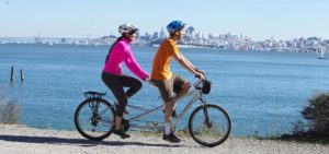 Two people riding tandem bike with San Francisco skyline in background